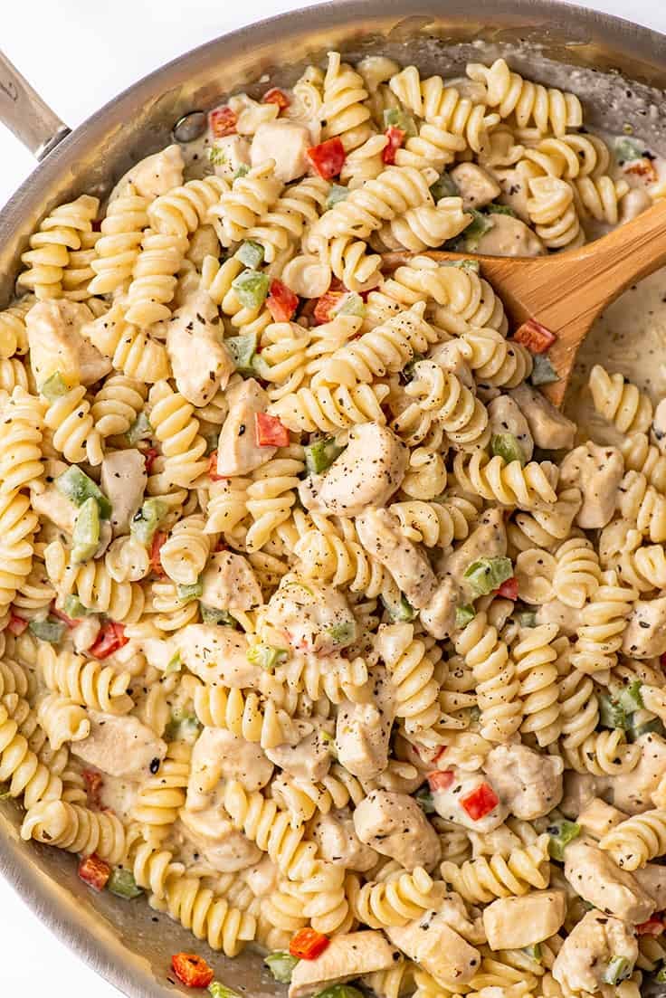 Spoon scooping creamy chicken pasta with bell peppers.