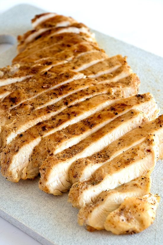Sliced cooked chicken breast for a salad on a cutting board.