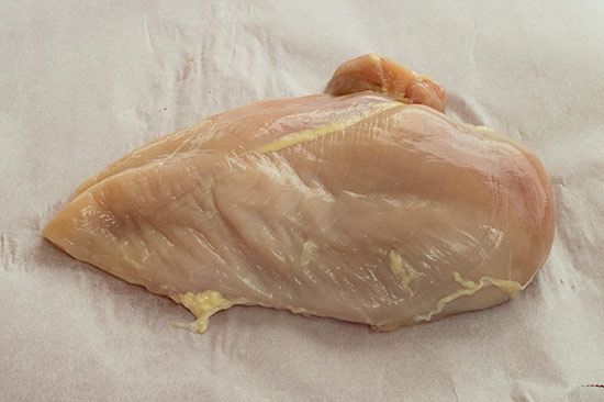 Raw boneless skinless chicken breast on parchment paper.