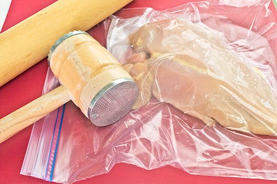 Chicken breast in a plastic bag with a meat mallet.