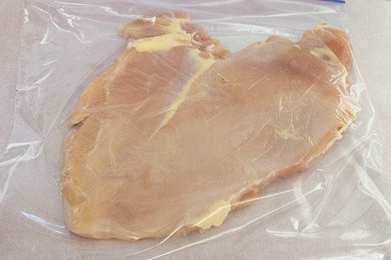 Chicken breast that's been pounded flat in a plastic bag.