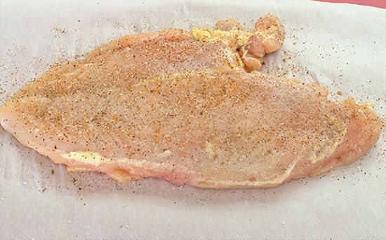 Chicken breast that's been pounded flat being seasoned with taco seasoning.