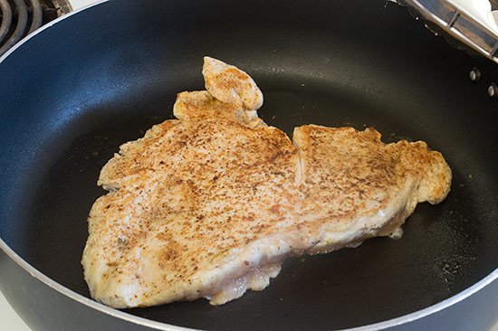 Chicken breast that's been pounded flat being cooked on the stove.