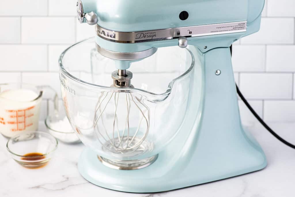 Stand mixer on a counter with whipped cream ingredients.