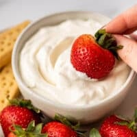Strawberry being dipped in whipped cream.
