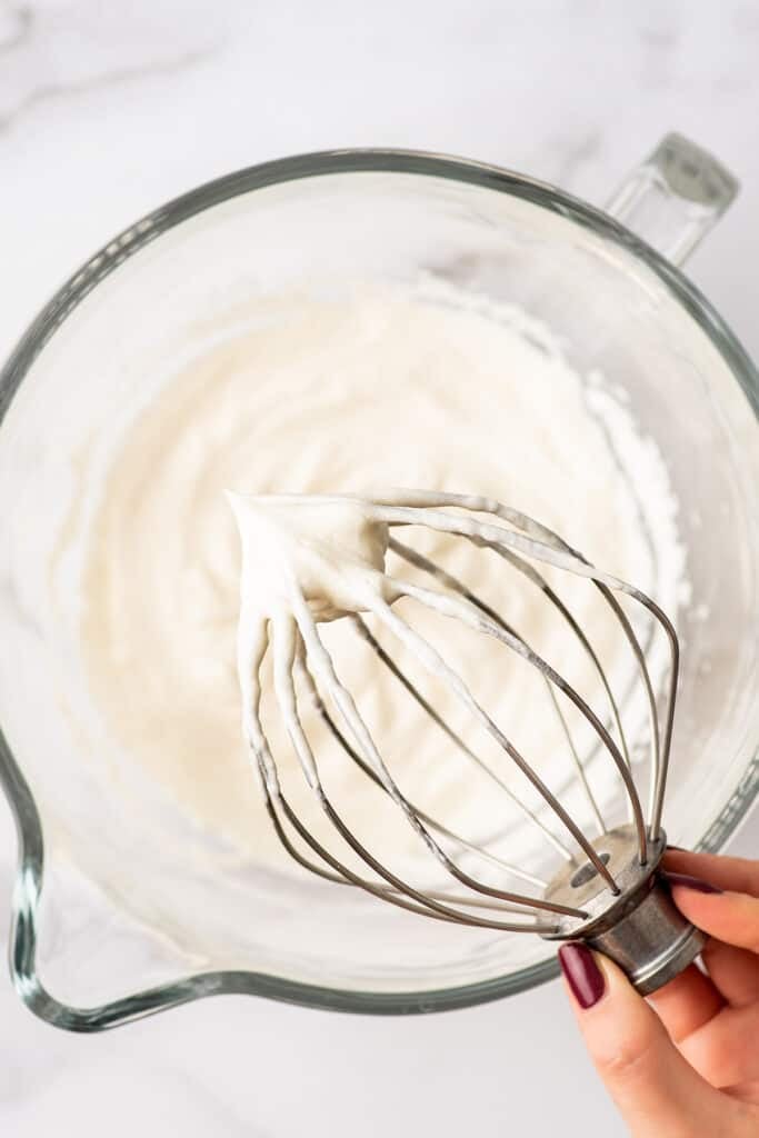 Stand mixer whisk attachment with whipped cream on it.
