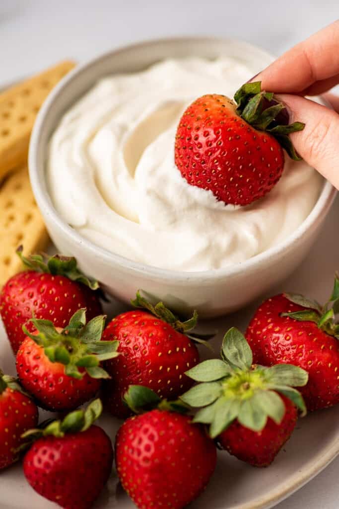 Strawberry being dipped in whipped cream.