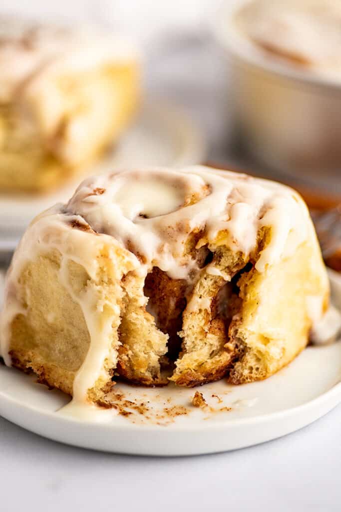 Overnight cinnamon roll on a plate with a bite out of it.