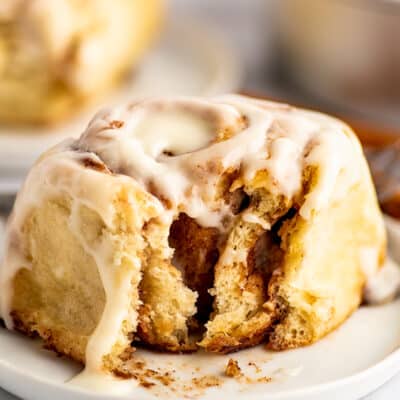 Overnight cinnamon roll on a plate with a bite out of it.