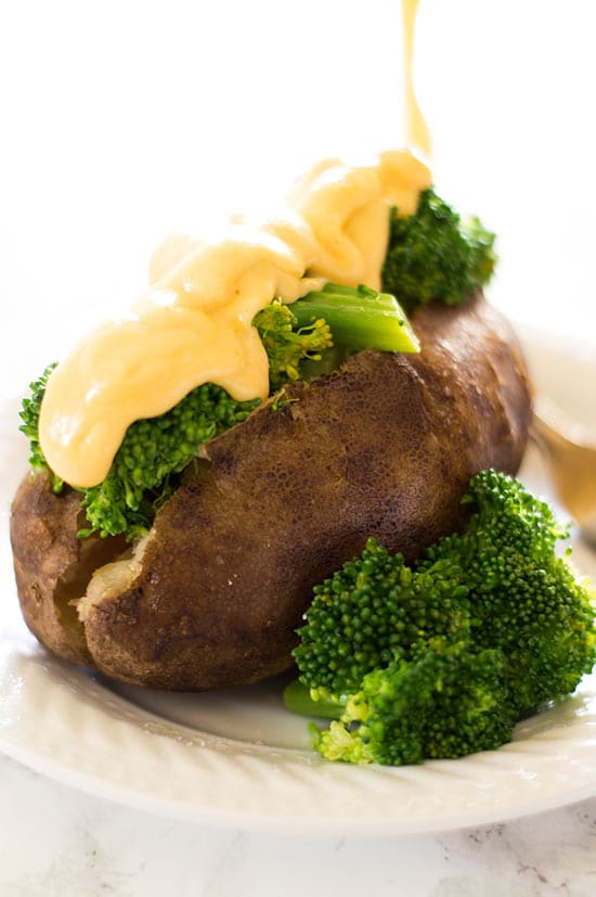 Cheese sauce being poured over broccoli and a slow cooker baked potato.