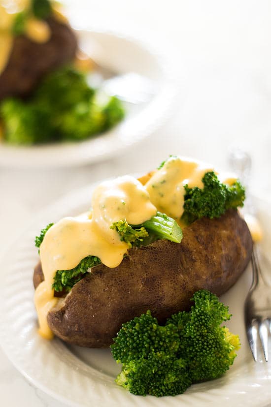 Slow cooker baked potato with broccoli and cheese sauce on a white plate.