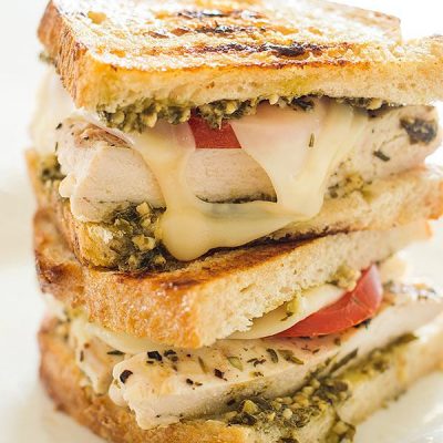 Pesto chicken sandwich halves stacked on a white plate.