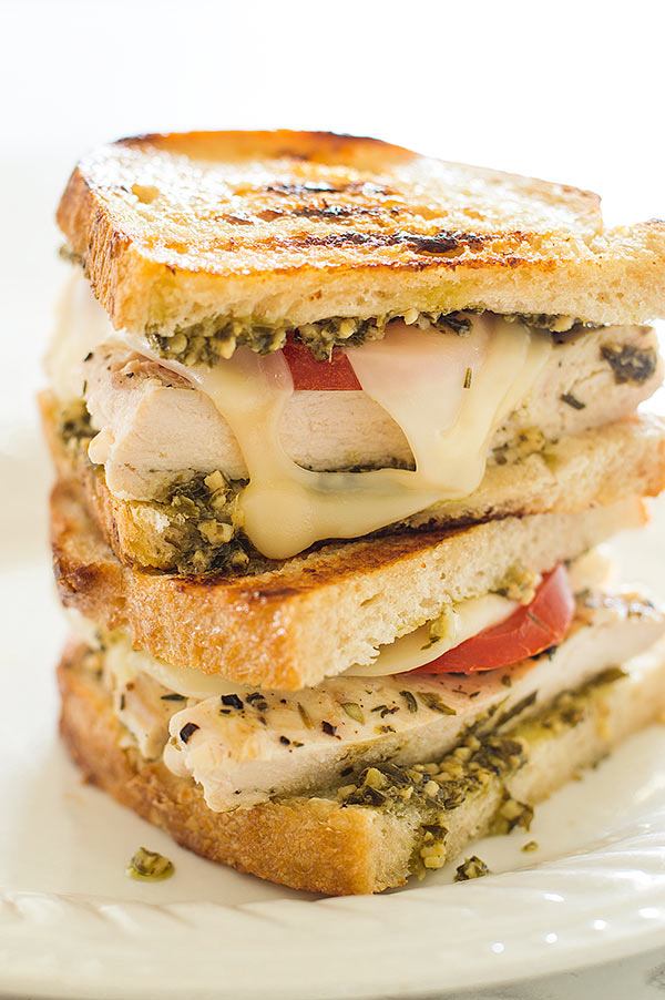 Pesto chicken sandwich halves stacked on a white plate.