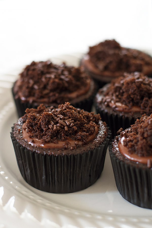 Insanely chocolatey Brooklyn Blackout Cupcakes made with three different types of chocolate, stuffed with a creamy chocolate pudding, and topped with sprinkles and a chocolate glaze. Recipe includes nutritional information. From BakingMischief.com