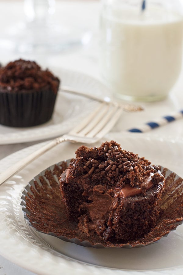 Insanely chocolatey Brooklyn Blackout Cupcakes made with three different types of chocolate, stuffed with a creamy chocolate pudding, and topped with sprinkles and a chocolate glaze. Recipe includes nutritional information. From BakingMischief.com