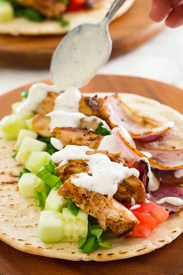 Yogurt shawarma sauce being spooned over chicken shawarma on a plate.