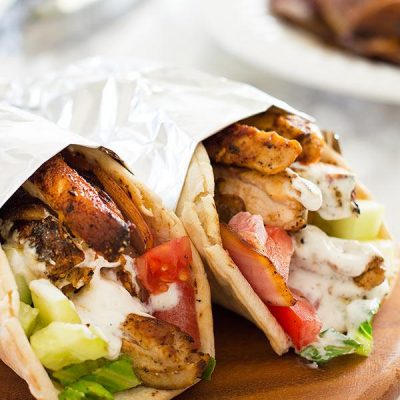 Chicken shawarma with yogurt shawarma sauce wrapped in foil on a wooden plate.