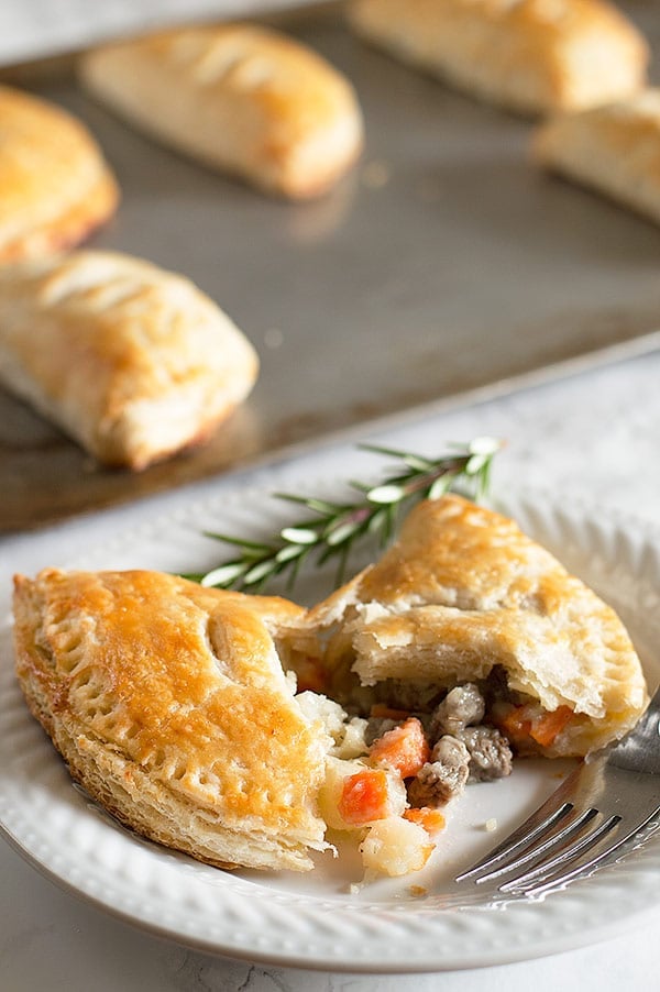 Beef pasties with one broken open on a white plate.