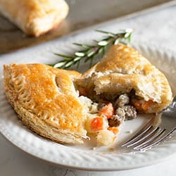 Beef pasties with one broken open on a white plate.