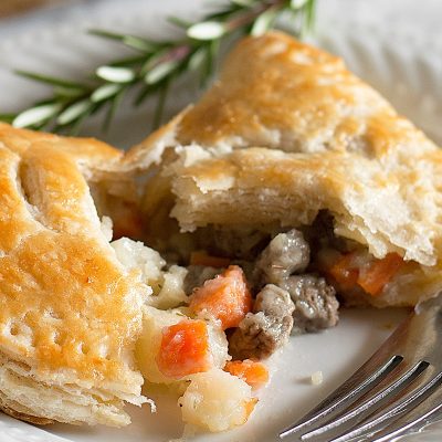 Beef pasties with one broken open on a white plate.