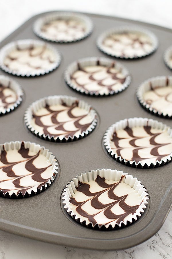 Mini mocha and Kahlua cheesecakes with a crunchy Oreo cookie base, cool sour cream topping, and fudge sauce. Recipe includes small-batch instructions and nutritional information. From BakingMischief.com