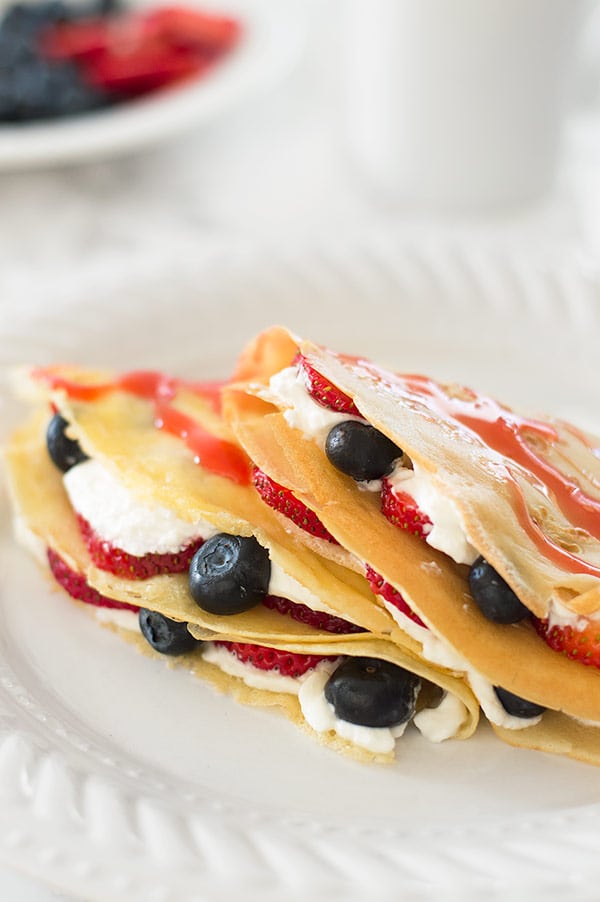 Crepes for two stuffed with whipped cream and berries on a white plate.