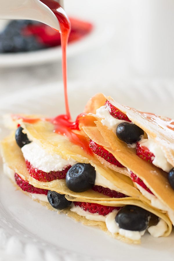 Strawberry syrup being poured over a plate of crepes for two.