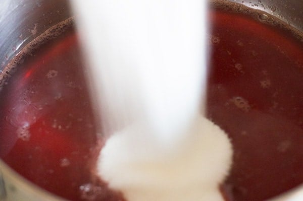 Sugar being poured into strawberry juice for strawberry syrup.