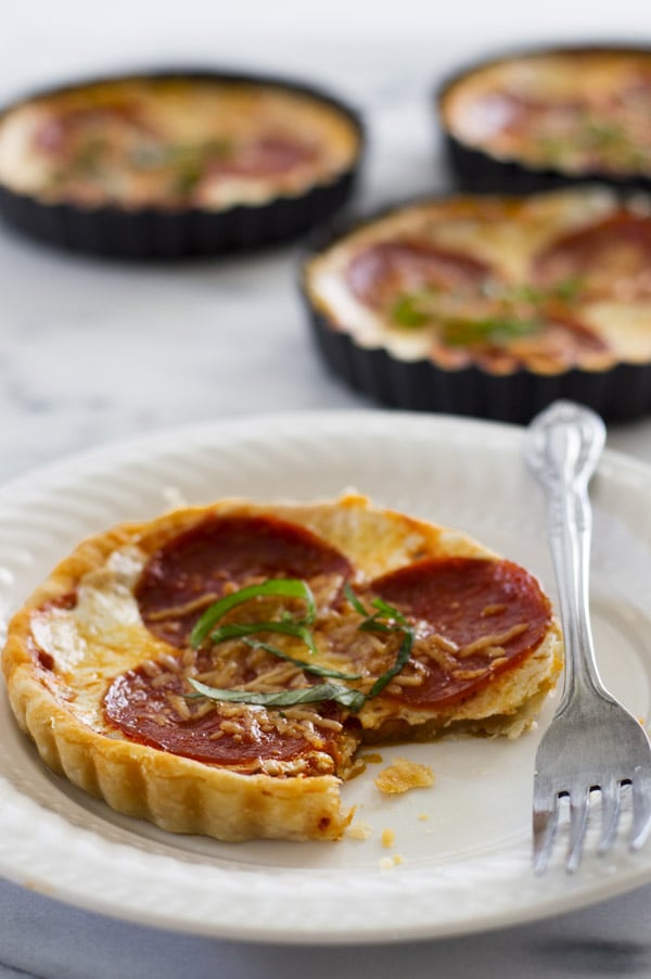 Pizza tart on a white plate with a bite out of it.