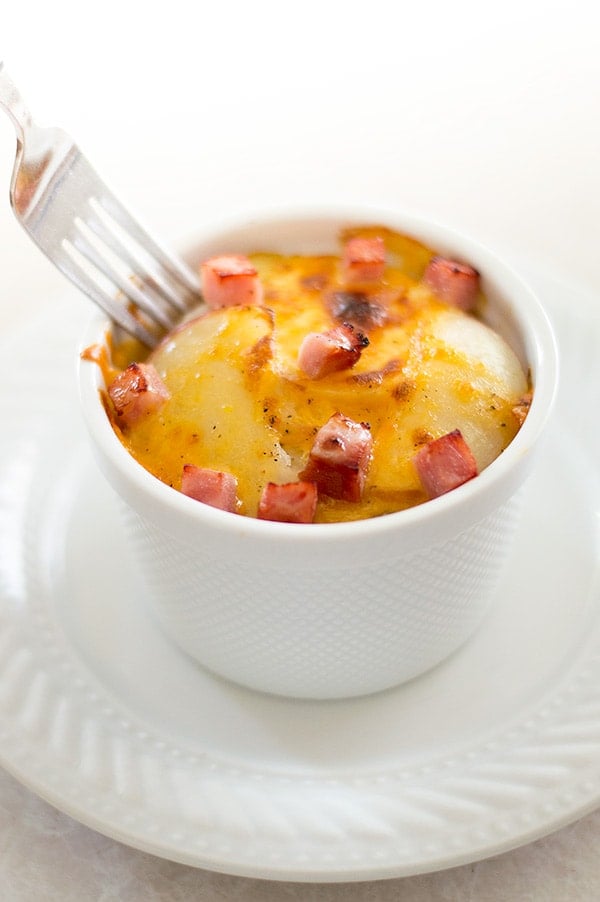 Scalloped potatoes in a white ramekin on a plate.