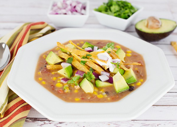 Chicken soup in a white bowl with avocado pieces.