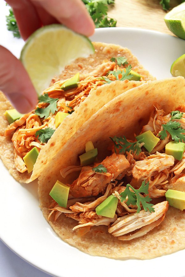 A lime being squeezed over sriracha chicken tacos.