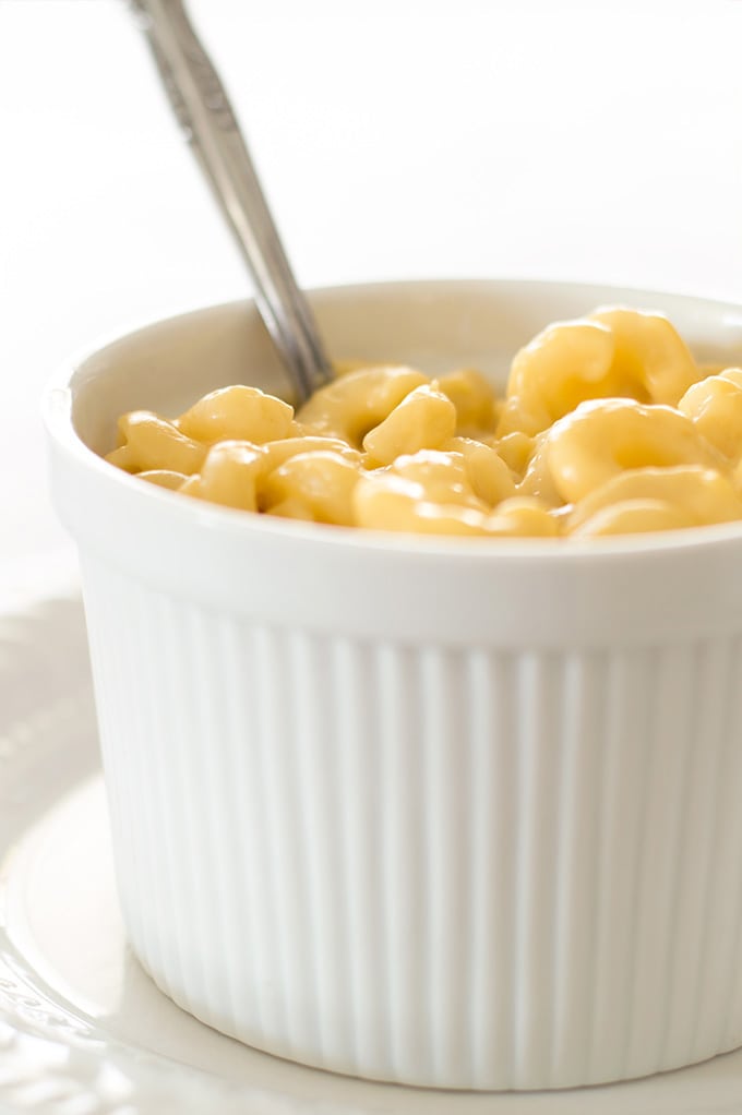 Close photo of mac and cheese for one in a white bowl with a spoon sticking out.