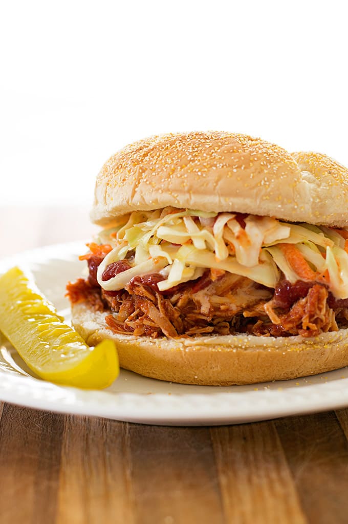 Slow cooker BBQ chicken sandwich on a plate with a pickle.