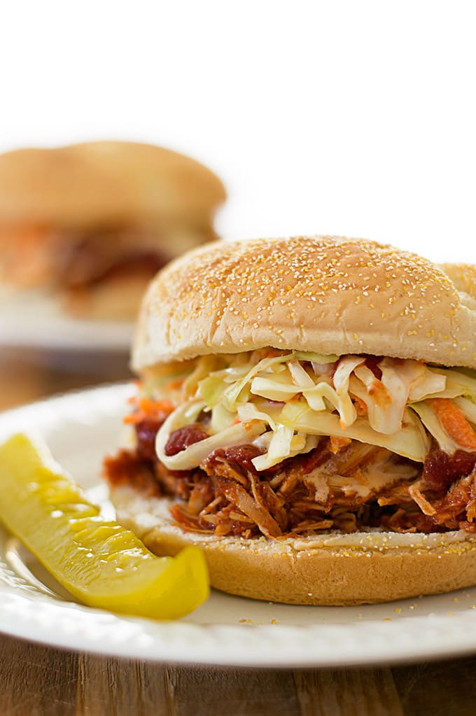 Slow cooker BBQ chicken sandwiches on a plate with a pickle.