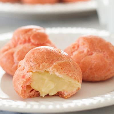 Pink cream puffs on a white plate.