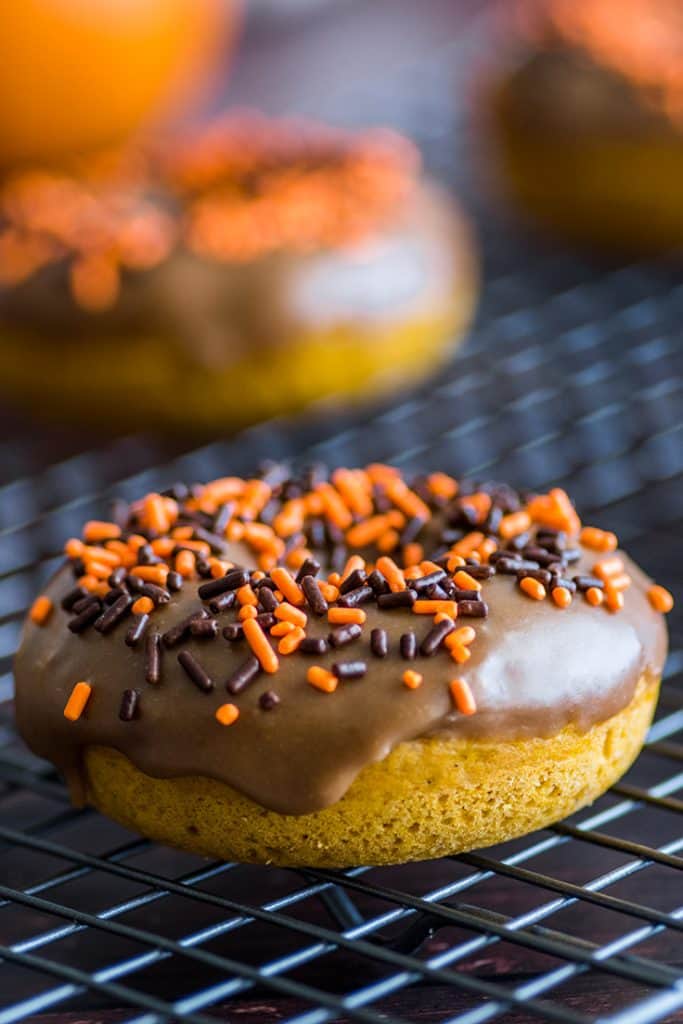 Baked pumpkin donut with maple glaze and sprinkles on a cooling rack.