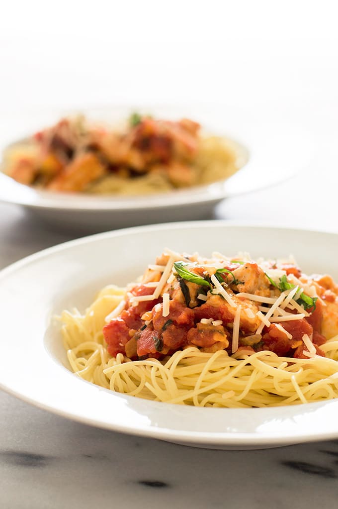 Photo of Basil Chicken Pasta over angel hair pasta in a white bowl.