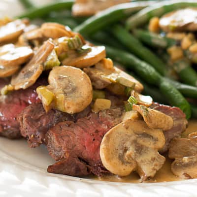 Top sirloin covered with mustard sauce and mushrooms on a plate with green beans.