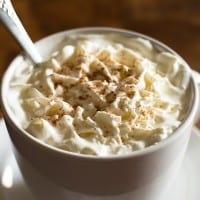 Eggnog latte with whipped cream in a white mug.