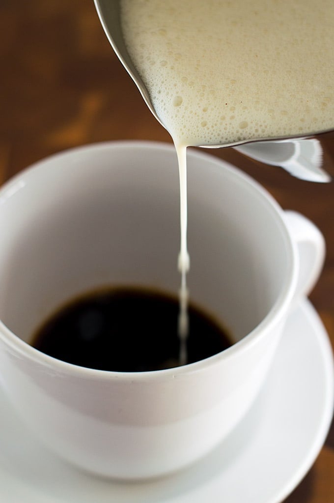 Milk for an eggnog latte being poured over coffee.