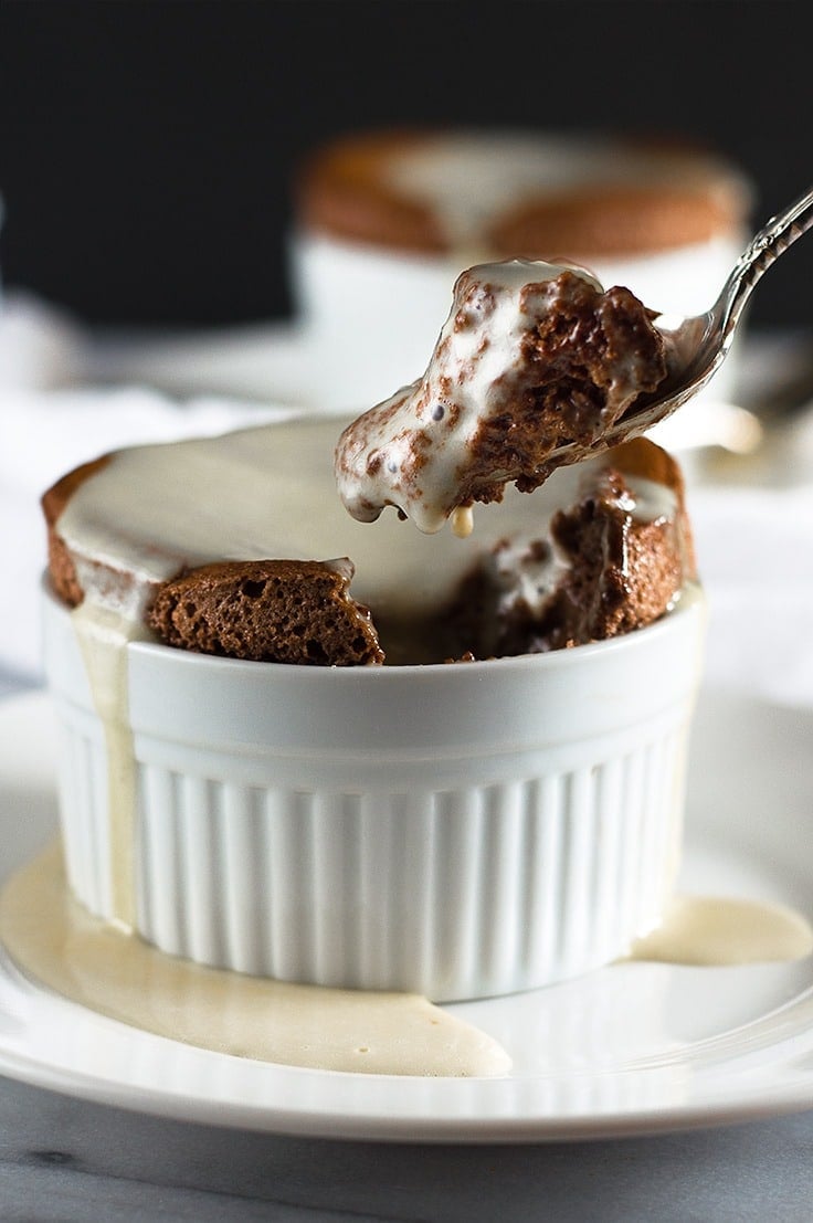 Fork taking a scoop out of a chocolate souffle in a white ramekin.