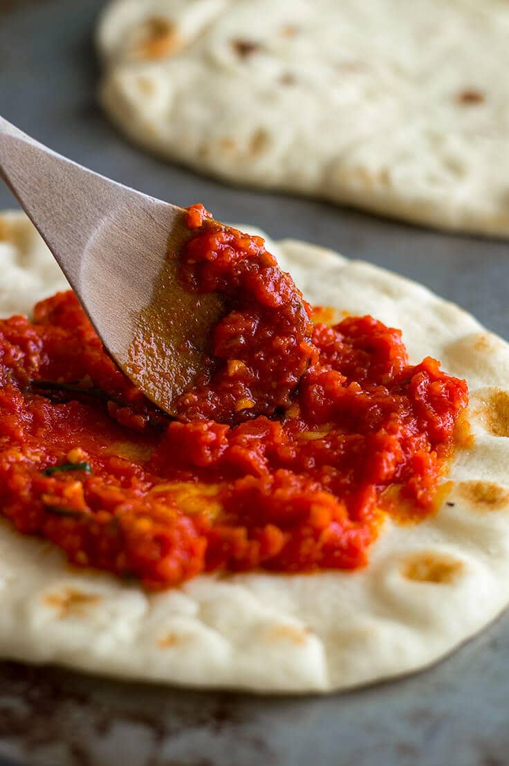Homemade pizza sauce being spread on naan pizza.