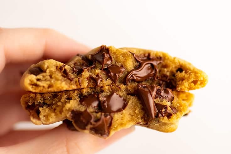 Hand holding a gooey chocolate chip cookie that's been split in half.