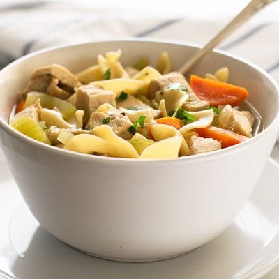 Photo of chicken noodle soup for one in a white bowl with a spoon.