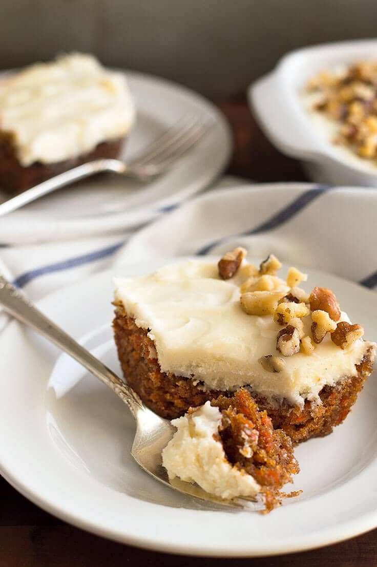 Picture of slice of small white carrot cake with cream cheese frosting on a white plate.