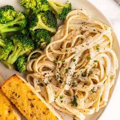 Fettuccine alfredo for one on a plate with broccoli and garlic bread.