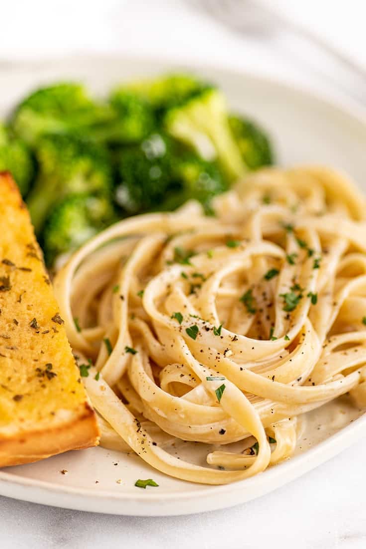 Single serve fettuccine alfredo on a plate with broccoli and garlic bread.
