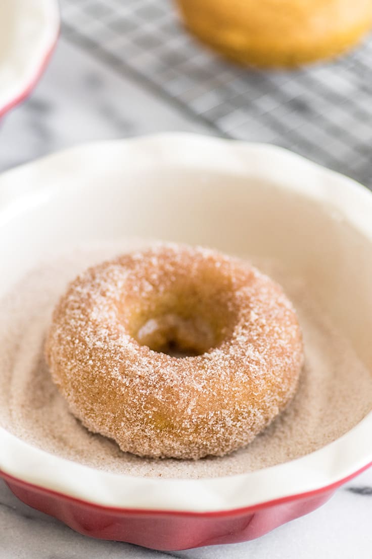 Picture of a Pumpkin Donut being dipped in cinnamon sugar.
