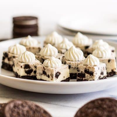Oreo cheesecake bites with whipped cream on a white plate.